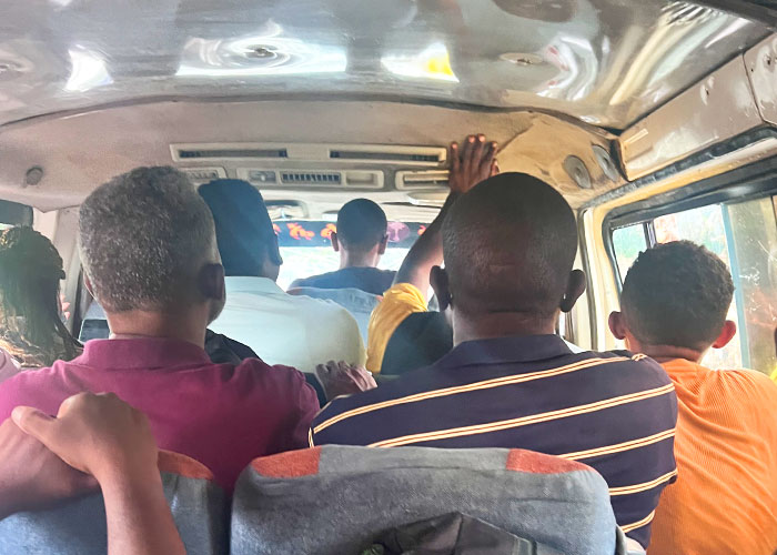 Six passengers in a van facing towards the driver and the road