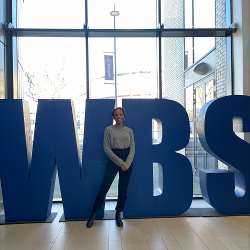 WBS student Odera standing in front of a WBS sign smiling at the camera
