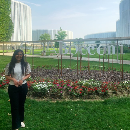 Akshada standing on some grass in front of a SDA Bocconi sign amongst some flowers