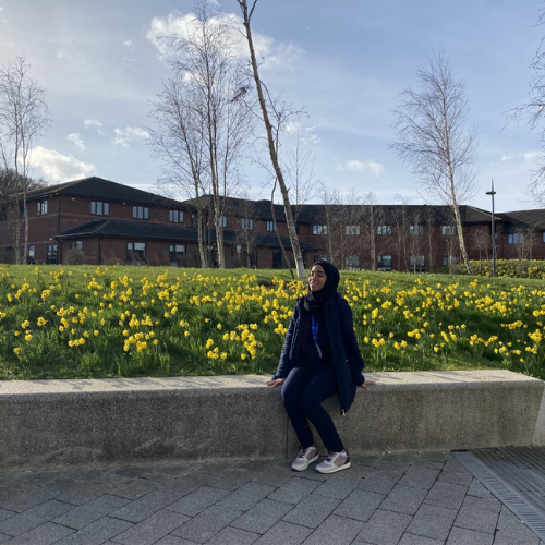 Hadeel sitting outside WBS on a sunny day, with daffodils in the background