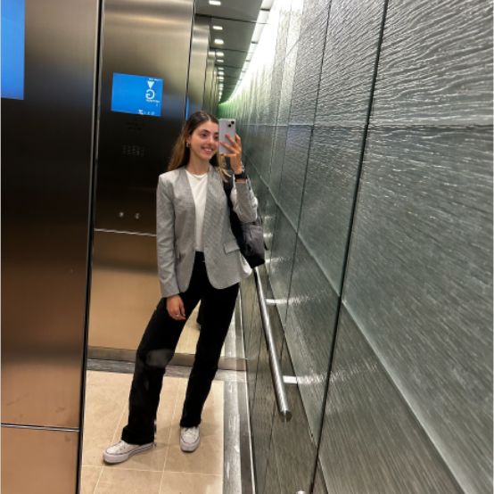 Julia taking a photo of her reflection in a mirror in a lift whilst smiling at the camera