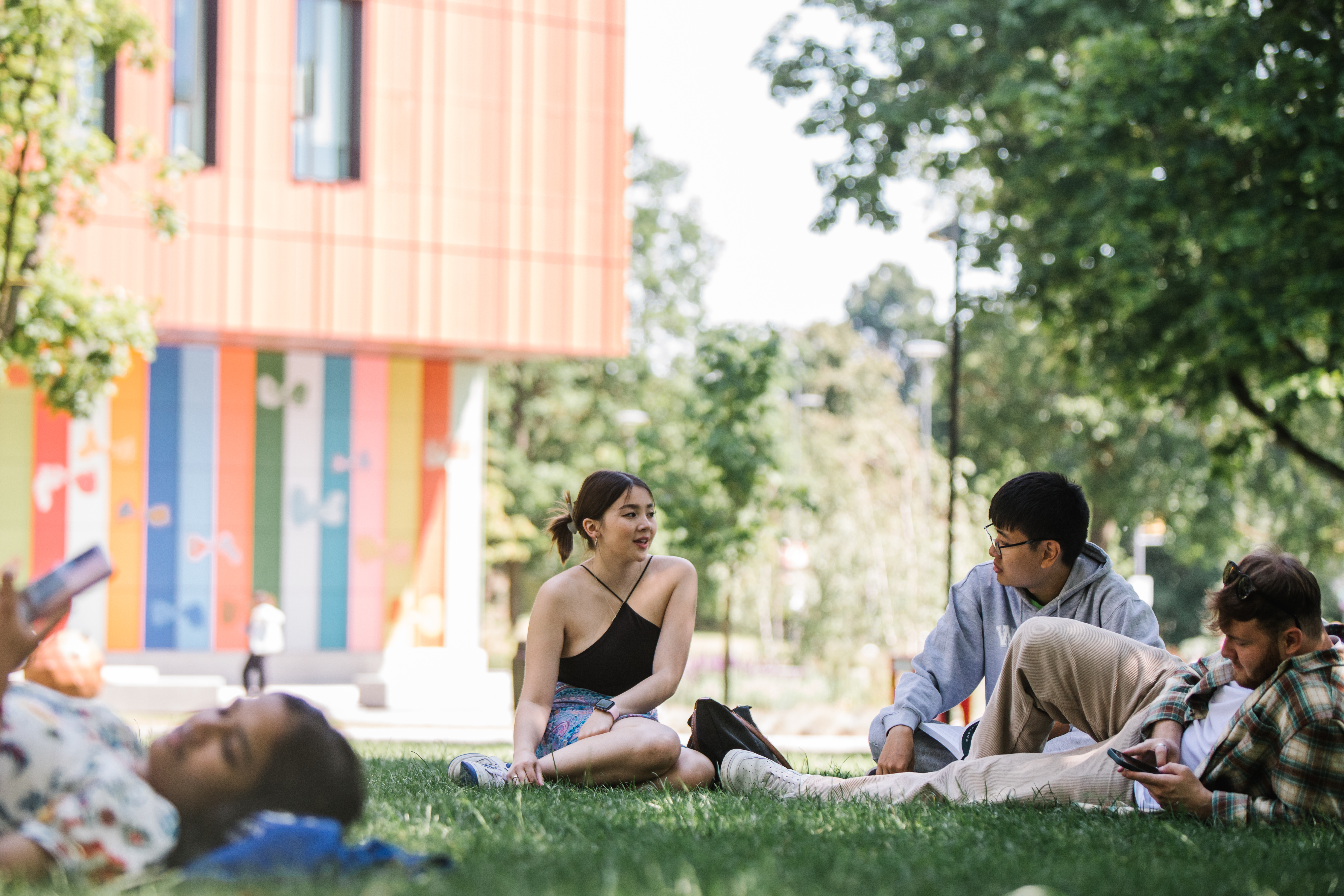 A group of students relaxing on an area of grass in front of a university building