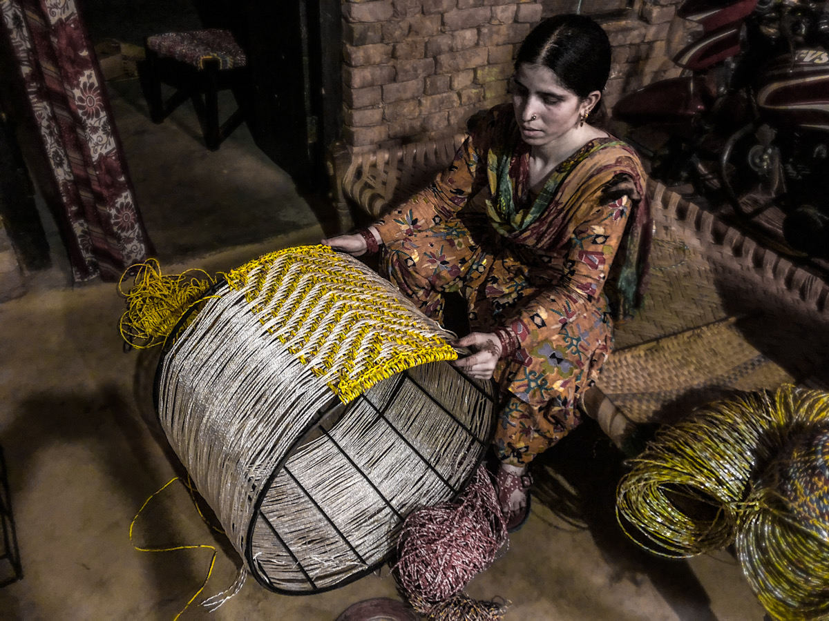 A women sat on a bench, weaving yellow thread onto a steel drum which is covered in silver thread