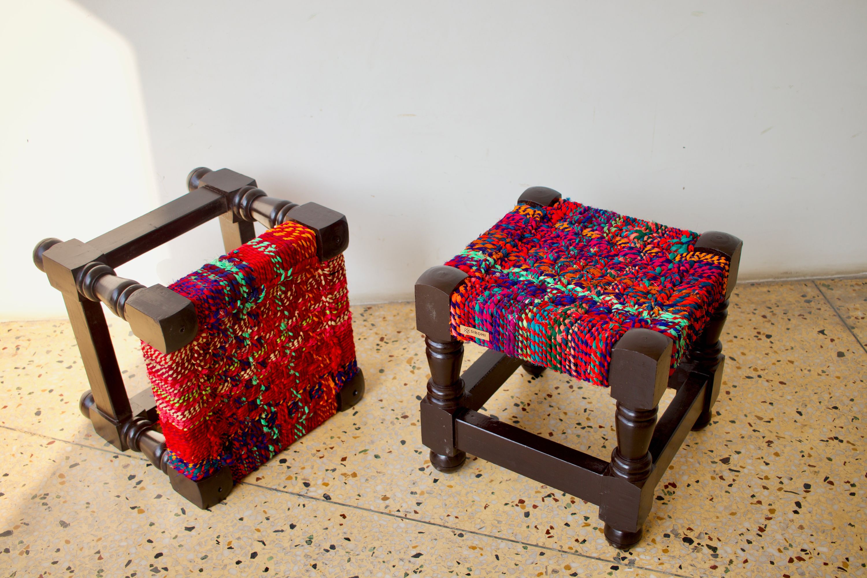 Two women dressed in traditional clothing weaving colourful thread to create a bench