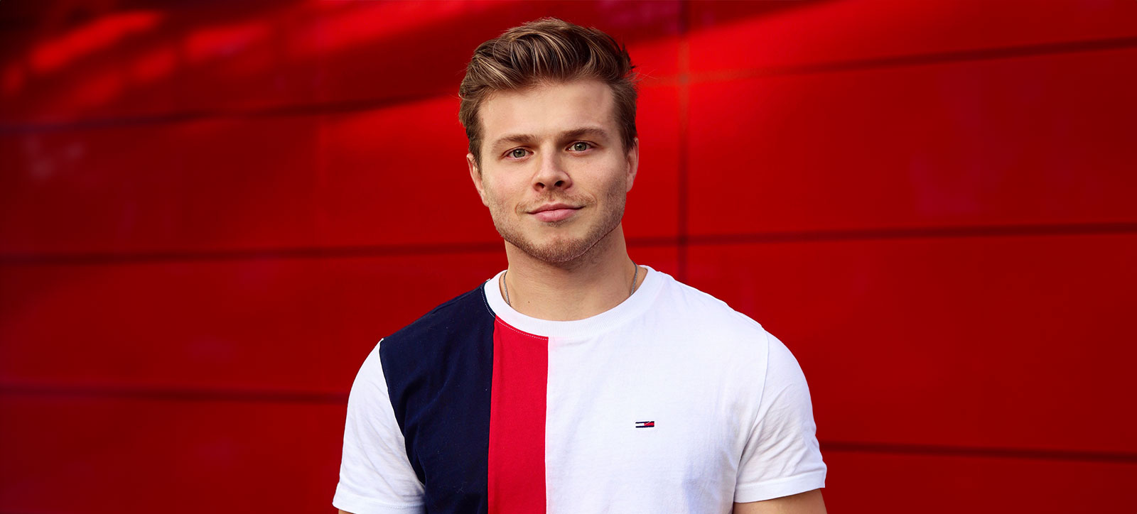 Max Klymenko, a WBS graduate, stood in front of a red background and smiling at the camera