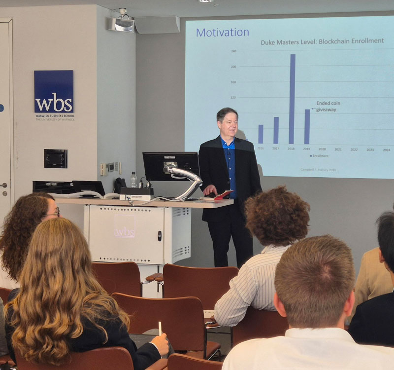 Professor Campbell Harvey of Duke University standing in front of a screen delivering the key note speech