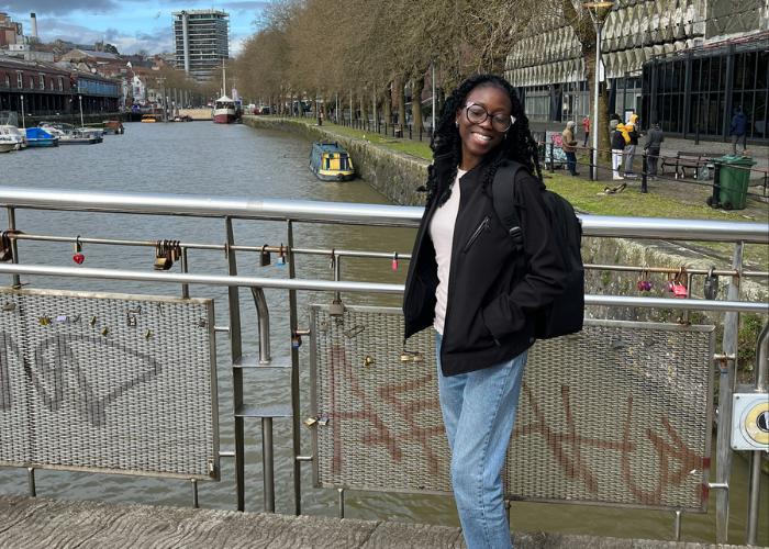 Bolu on a bridge smiling at the camera with a river and commercial buildings in the background