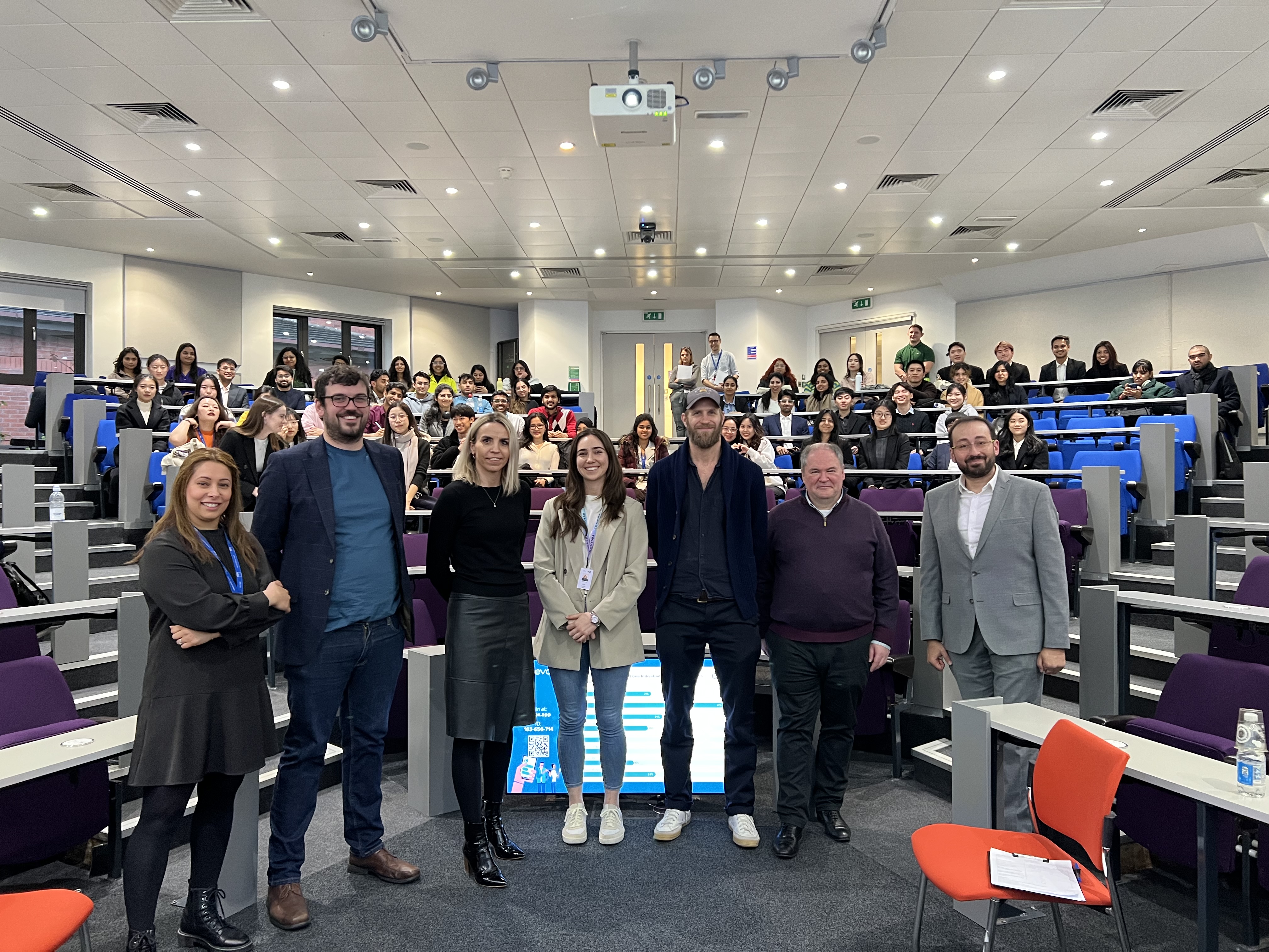 A panel of seven people stood in a lecture theatre with students sat behind them at their desks