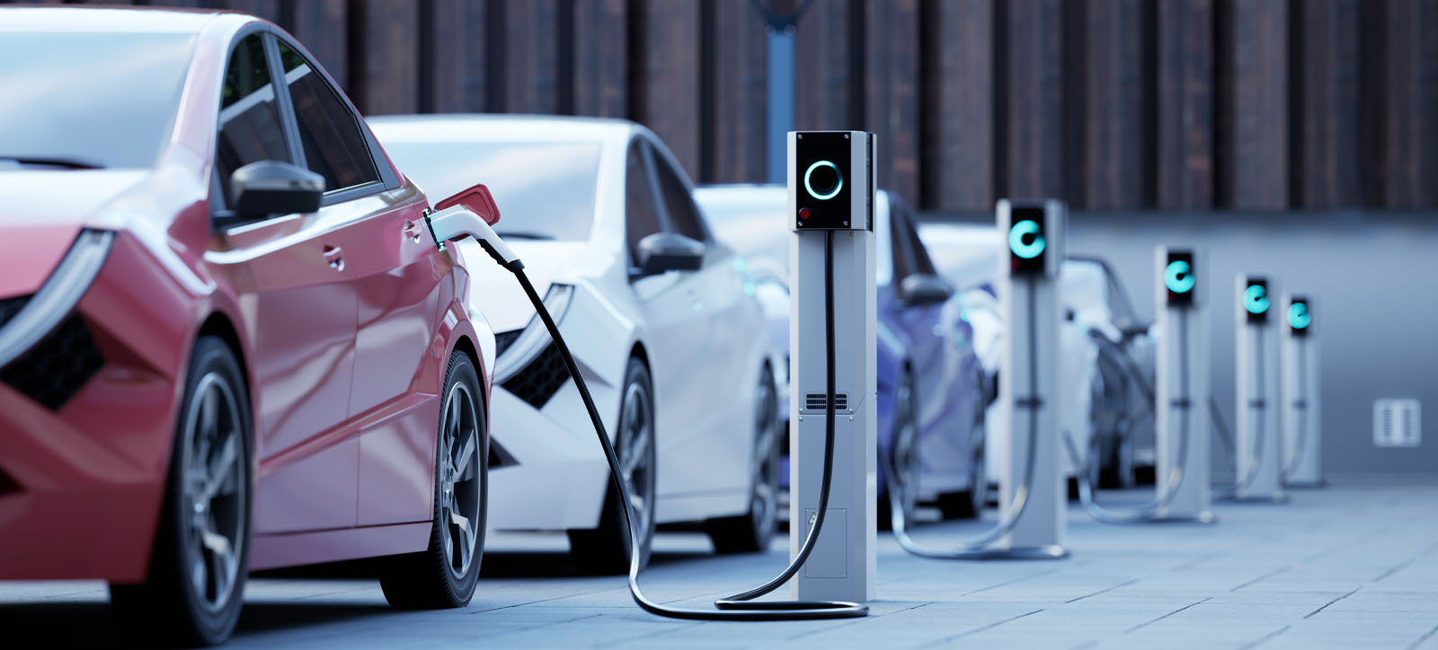 White electric cars lined up alongside the side of the street, all plugged into charging points
