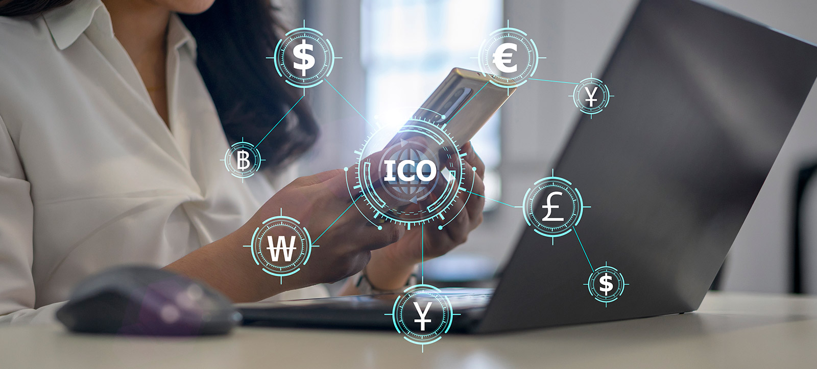A close up of a businesswomen sat at her desk with her laptop open, holding her smartphone in her hand. The icons for a range of digital currencies, each pegged to blockchain, can be seen emerging from the phone.