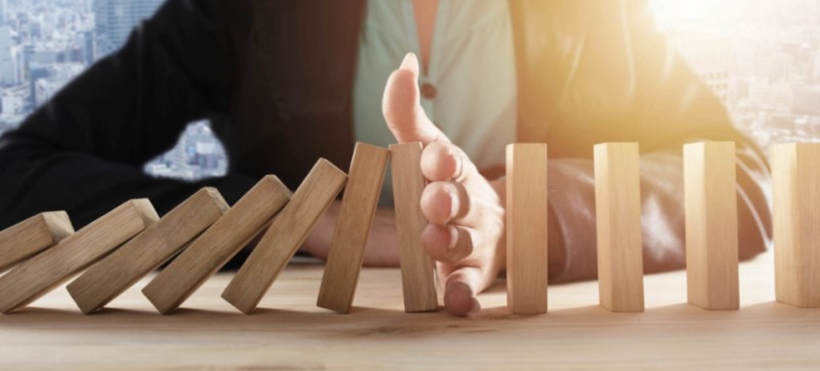 A female manager in a suit uses her hand to break a chain of toppling dominos. A female manager in a suit uses her hand to break a chain of toppling dominos.
