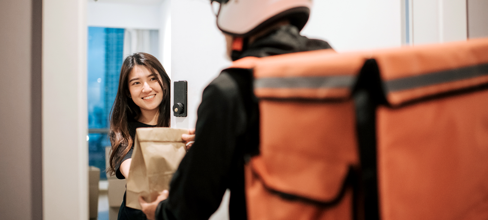 A delivery driver hands a food order to a customer on their doorstep A delivery driver hands a food order to a customer on their doorstep