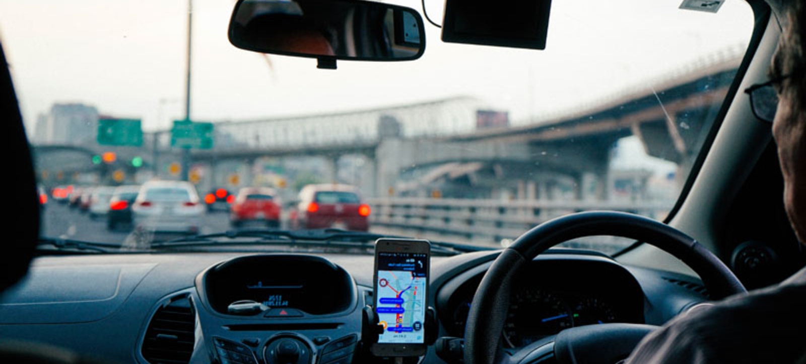 A person driving a car in traffic with a mobile phone displaying a navigational map application. A person driving a car in traffic with a mobile phone displaying a navigational map application.