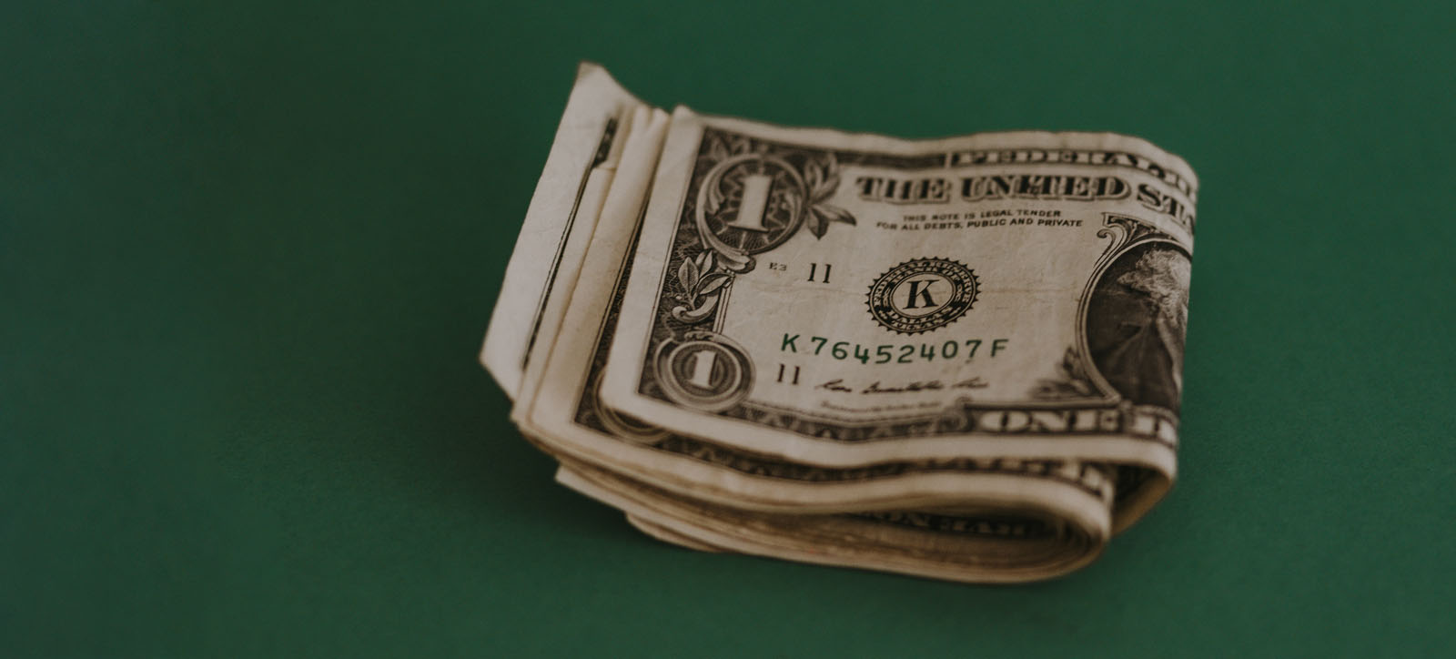 A rolled up stack of United States one-dollar bills against a dark green background.