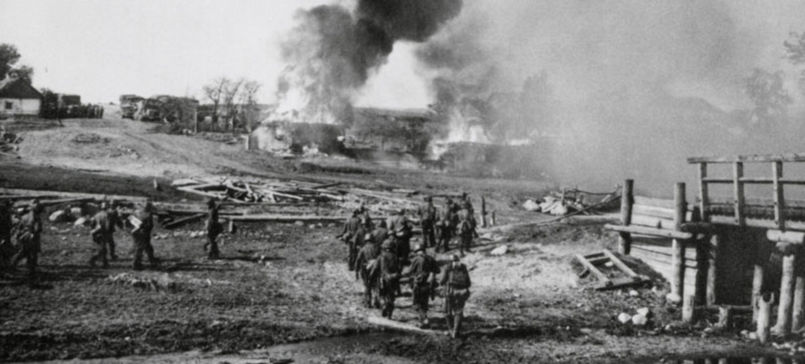 A group of soldiers in the Second World War walking across a battlefield with buildings covered in smoke in the background. A group of soldiers in the Second World War walking across a battlefield with buildings covered in smoke in the background.