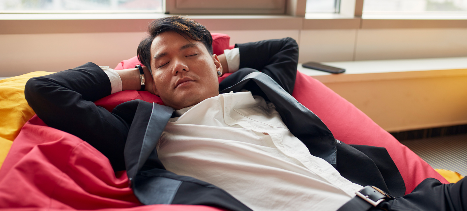A worker in a suit enjoys an afternoon nap in the office.