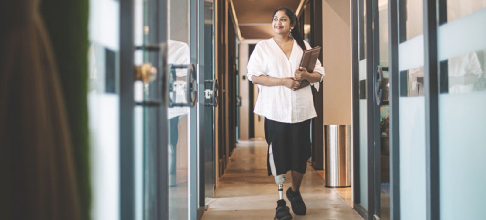 A worker with a prosthetic leg walks along an office corridor.