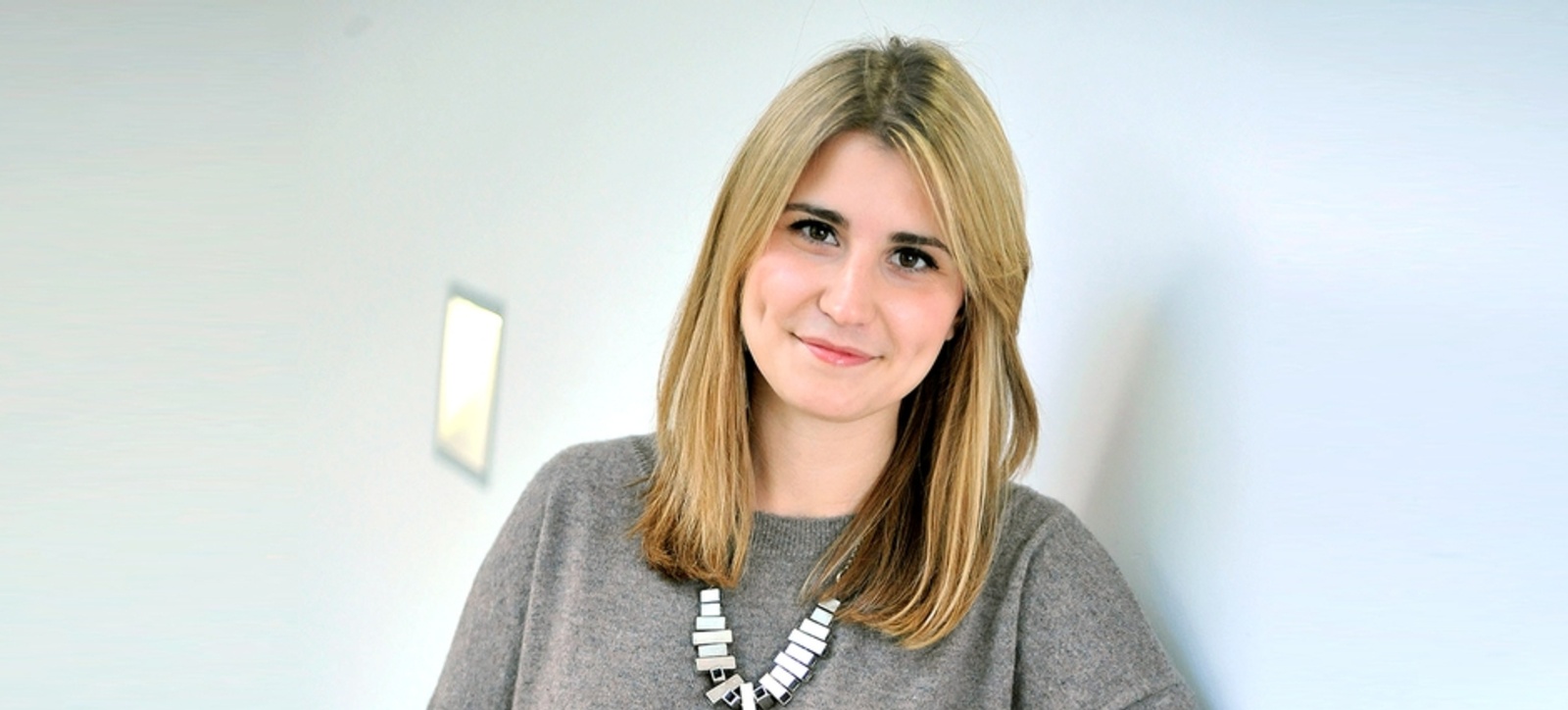 A women standing in front of a white coloured wall, smiling at the camera. A women standing in front of a white coloured wall, smiling at the camera.
