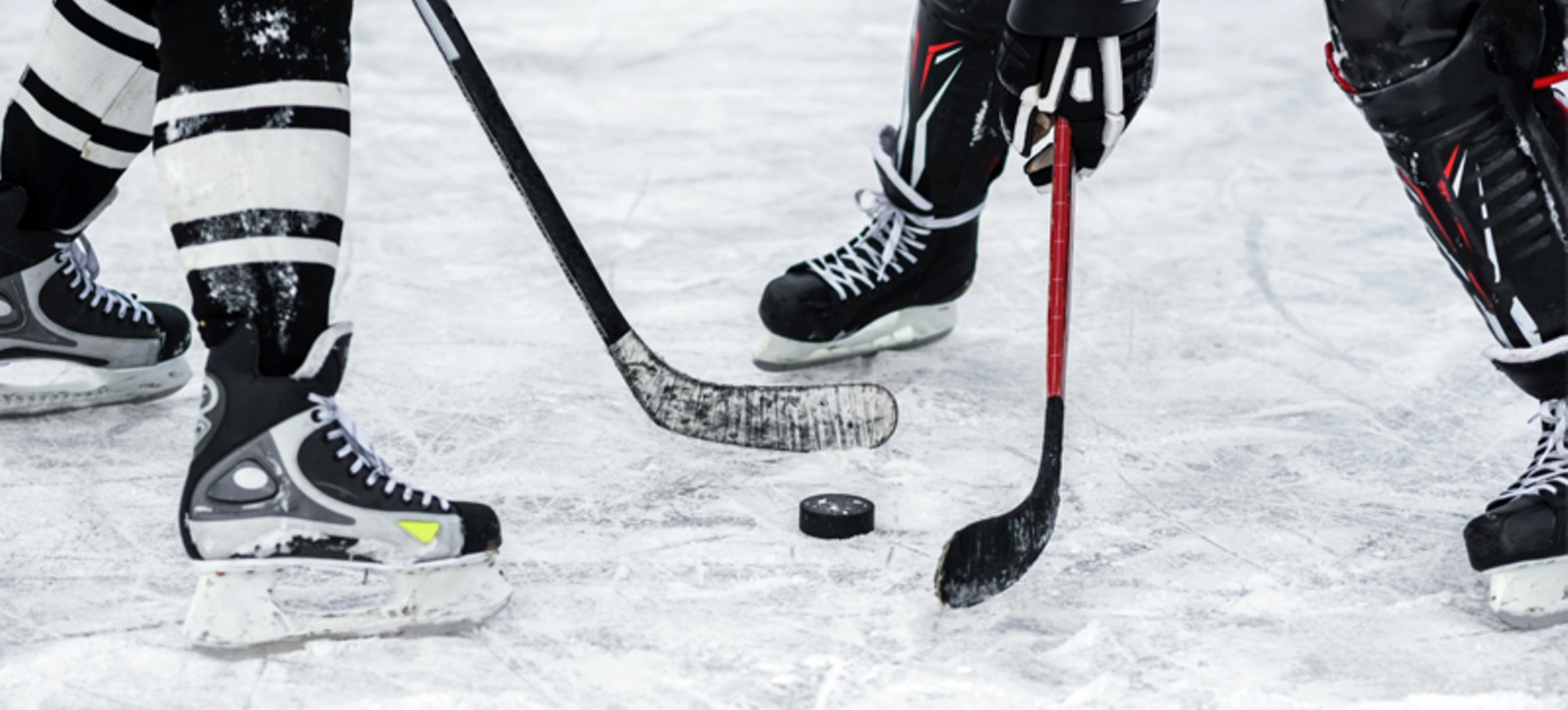 A close up of two ice hockey players facing off over a puck. A close up of two ice hockey players facing off over a puck.
