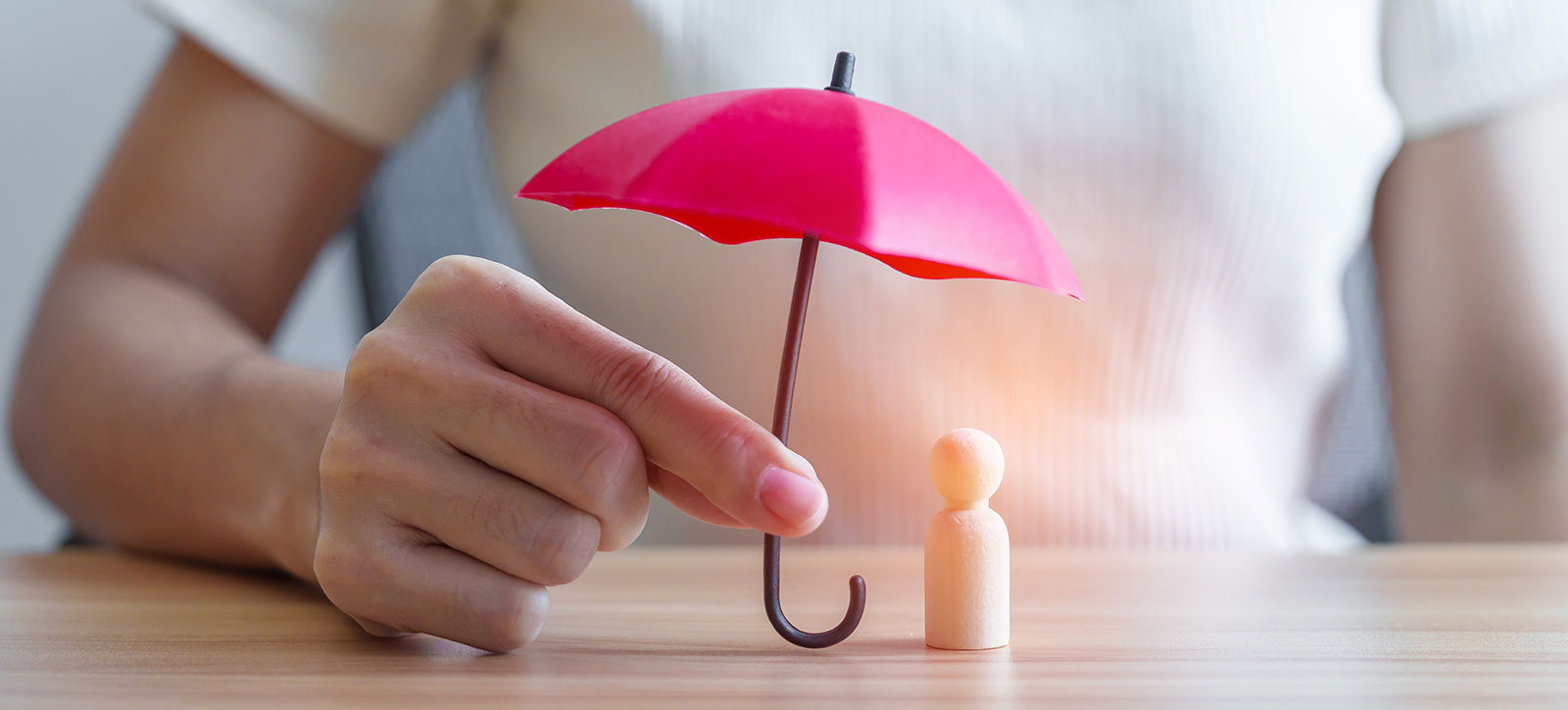A manager holds a tiny umbrella over a small wooden figure of a human that represents a worker, shielding them from the stress raining down on them.