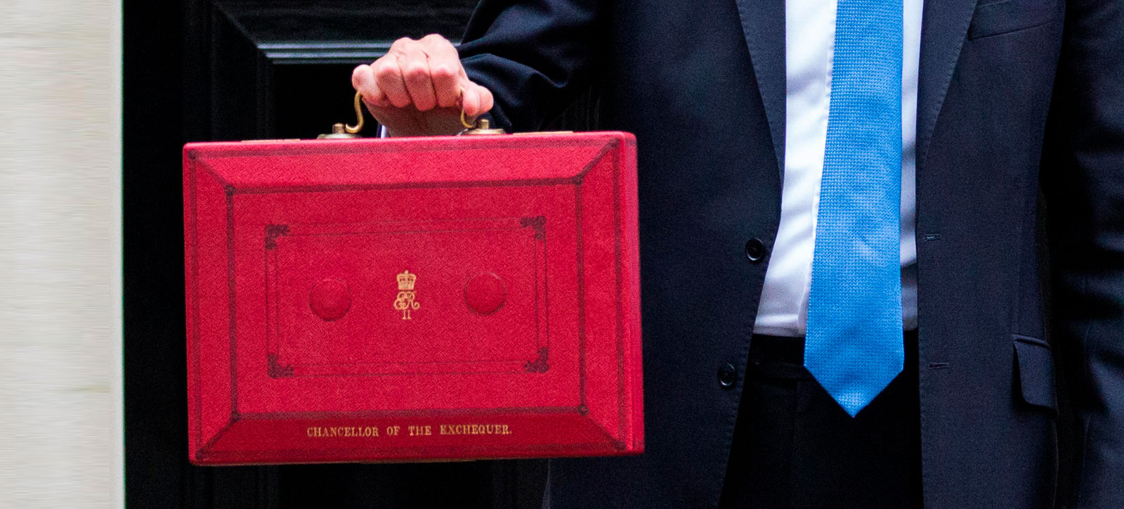 A close up of the Chancellor of the Exchequer's red briefcase containing the Budget, being held up outside the black front door of Number 10 Downing Street.