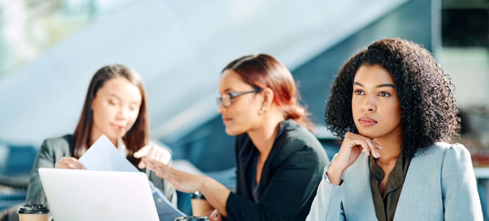 A Black office worker sits on the periphery of a meeting, starting into space, as she is ignored by her colleagues. A Black office worker sits on the periphery of a meeting, starting into space, as she is ignored by her colleagues.