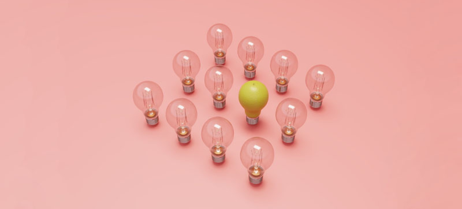 12 lighbulbs arranged in a four by four square formation. 15 are dim and unlit. The final one has been replaced by an upturned pair, creating the illusion of a lit lightbulb inside the group. The bulbs are stood up on a light pink background.