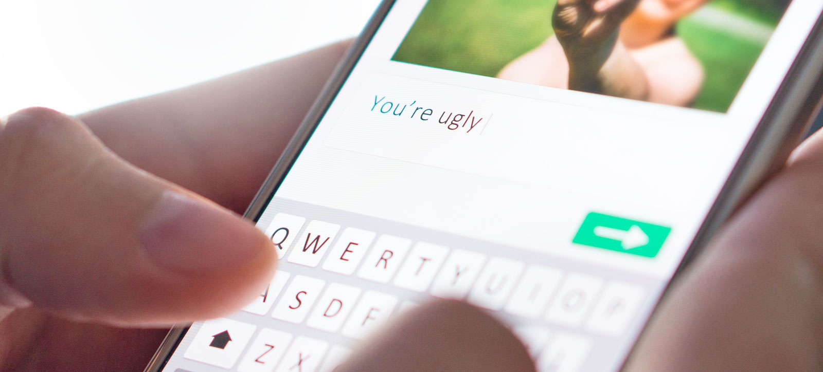 A close up of a hand typing an abusive message into a social media platform on a mobile phone.