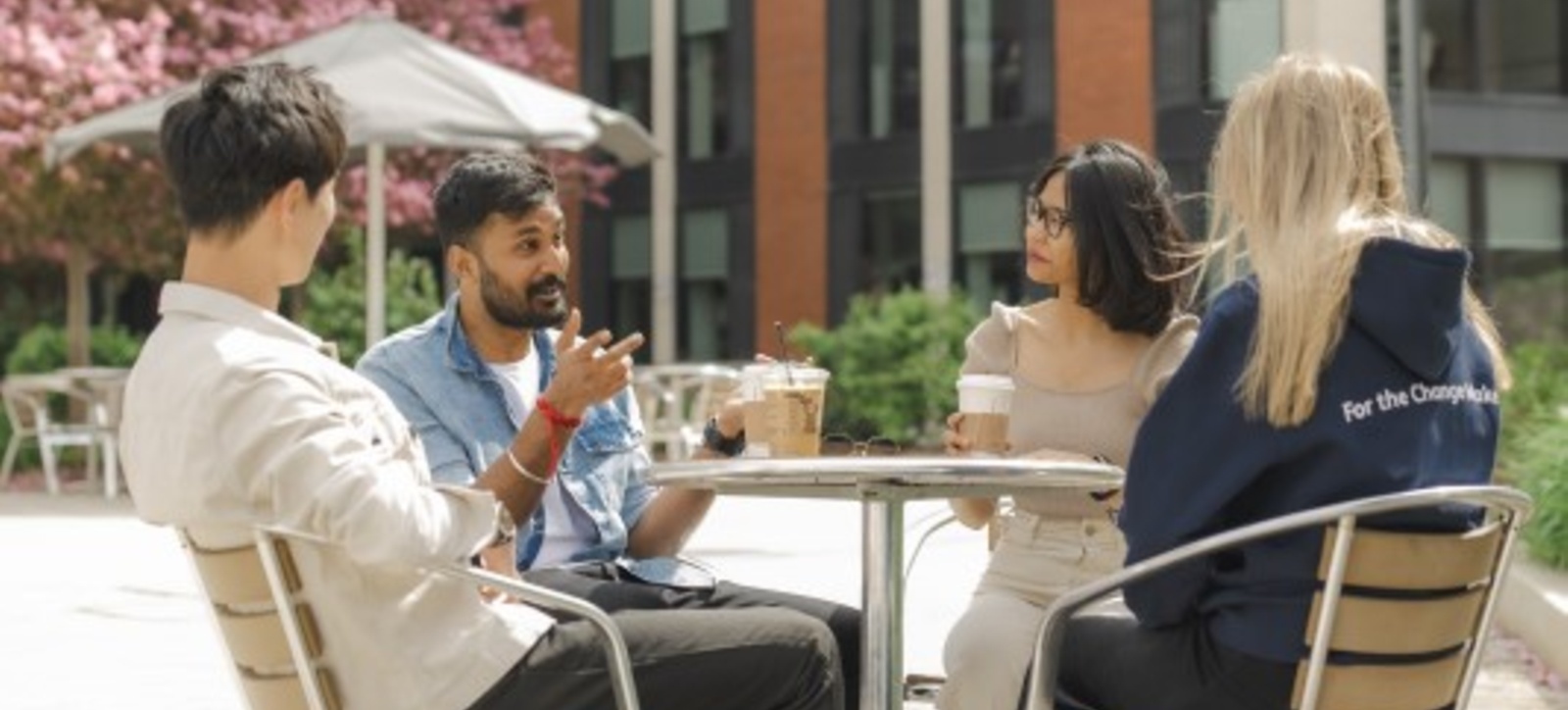 Four WBS students from the Foundation Year sitting around the cafe table outside Four WBS students from the Foundation Year sitting around the cafe table outside