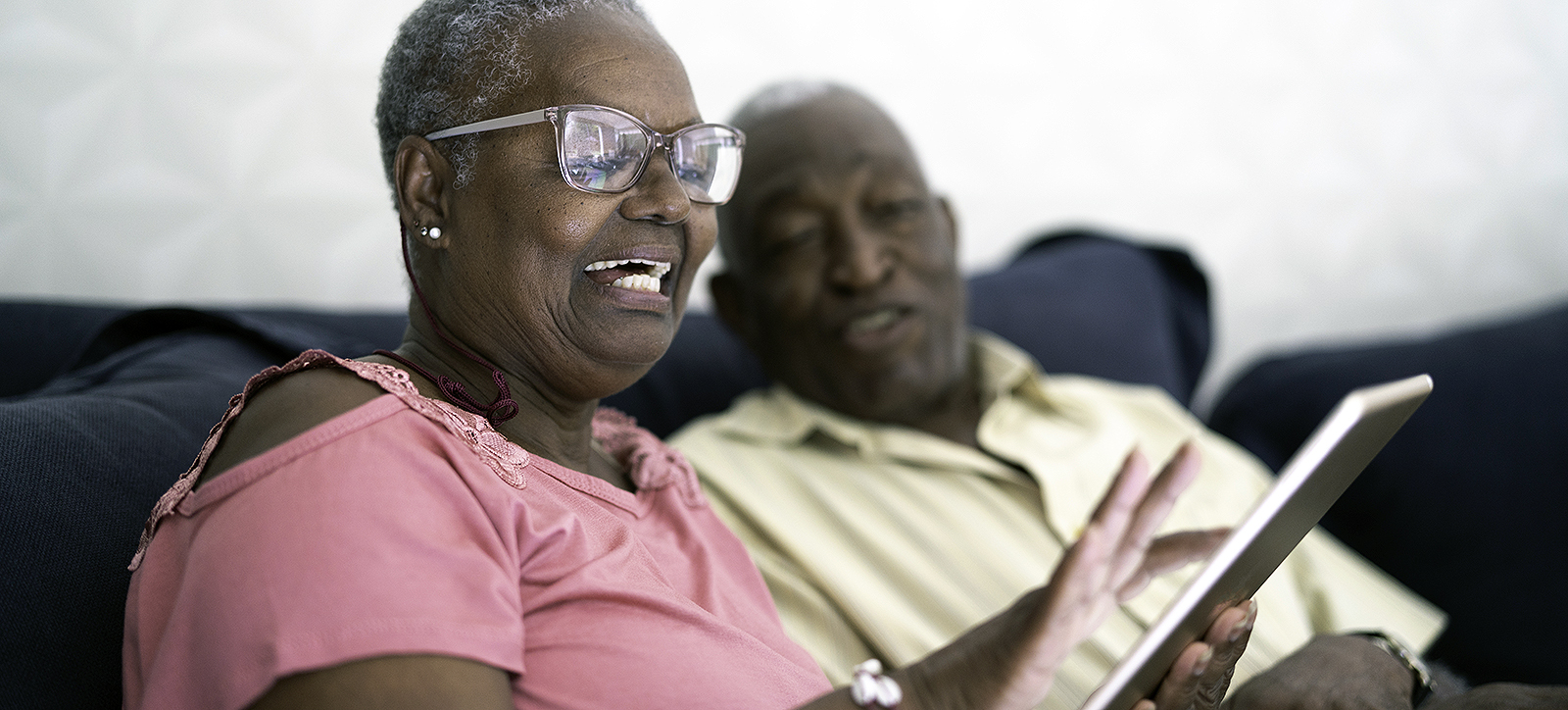 Two older people sat on the sofa using social media on a tablet.