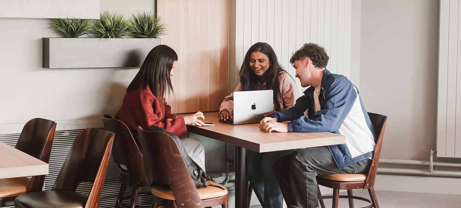 Three students, two female, one male looking and smiling at the screen of a laptop computer