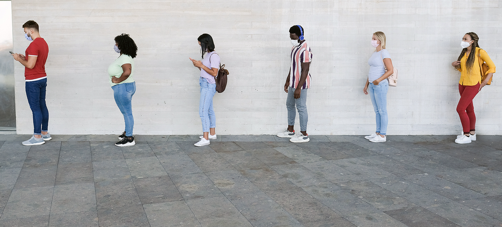 Young adults wear face masks while standing in a socially distance queue, showing how rapidly behaviour changed during the pandemic