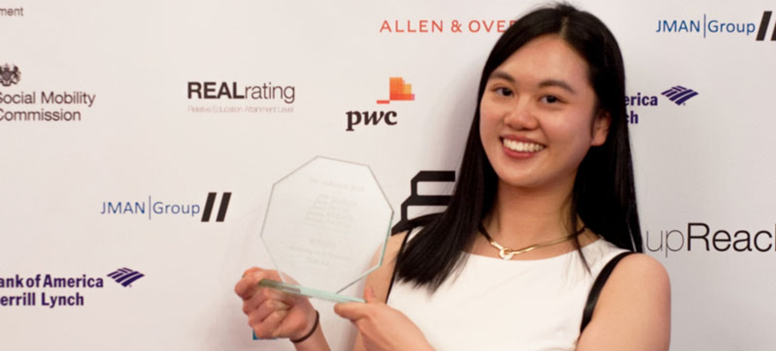 Suet Au stood in front of a media backdrop holding an award and smiling at the camera. Suet Au stood in front of a media backdrop holding an award and smiling at the camera.