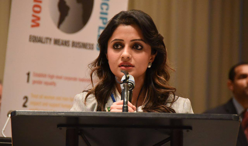 Fiza Farhan delivering a presentation while holding a microphone and standing behind a lectern. Fiza Farhan delivering a presentation while holding a microphone and standing behind a lectern.