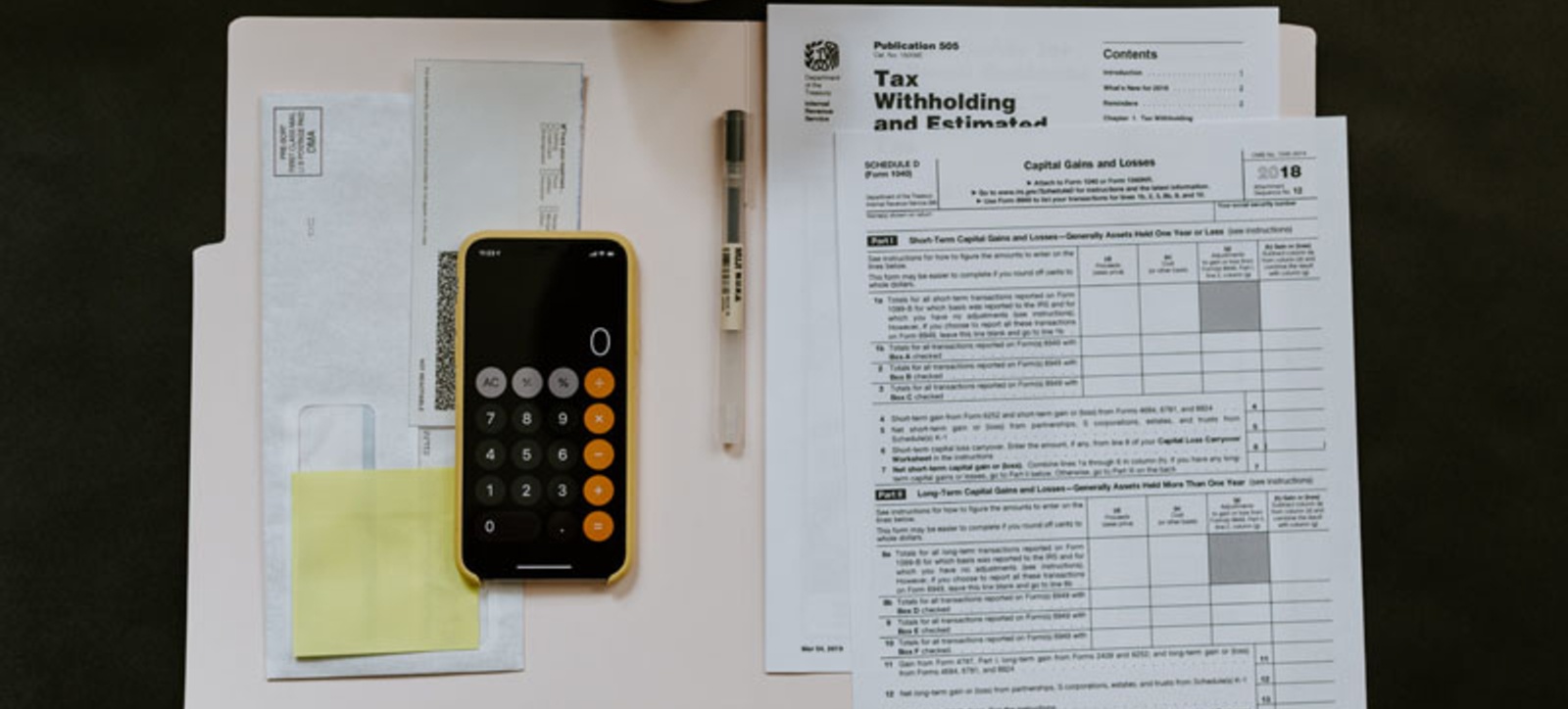 An open file on a desk with a phone displaying a calculator and collection of tax documents. An open file on a desk with a phone displaying a calculator and collection of tax documents.