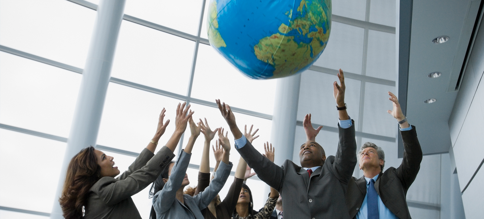 A diverse group of business men and women with their arms in their air to catch and inflatable global representing environmental and social issues A diverse group of business men and women with their arms in their air to catch and inflatable global representing environmental and social issues