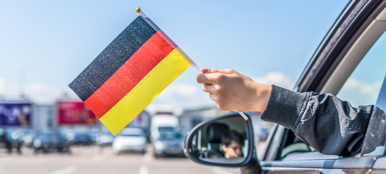 A photograph of child's hand hanging out of an open car window, holding a German flag in their hand. A photograph of child's hand hanging out of an open car window, holding a German flag in their hand.