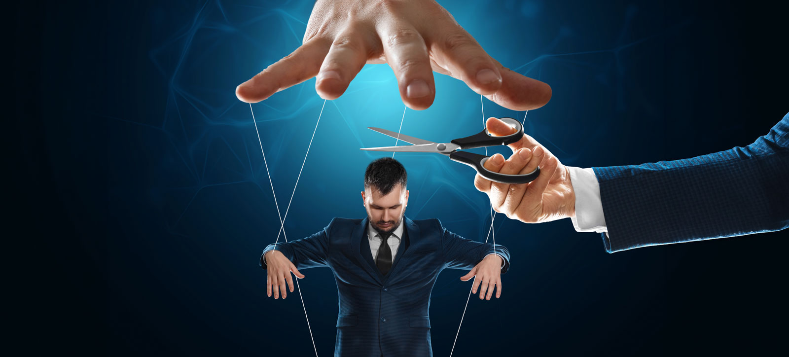A business leader wearing a suit uses a pair of scissors to cut the puppet strings holding an office worker in place