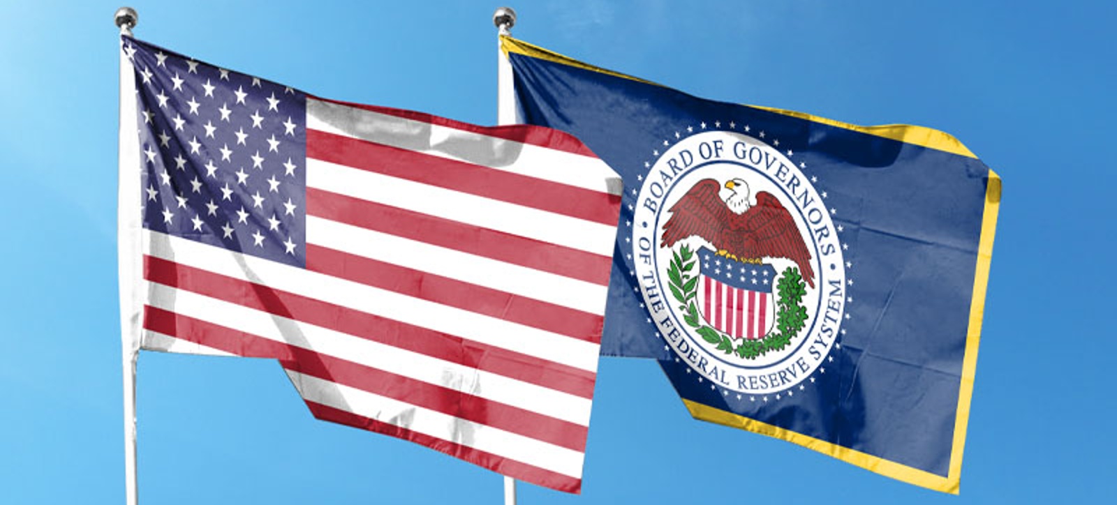 The flags of the United States (US) and the Federal Reserve Bank fly side by side from flagpoles, against a clear blue sky in the background.