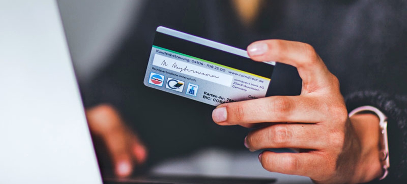 A close-up of a credit card being held by a person using a laptop. A close-up of a credit card being held by a person using a laptop.