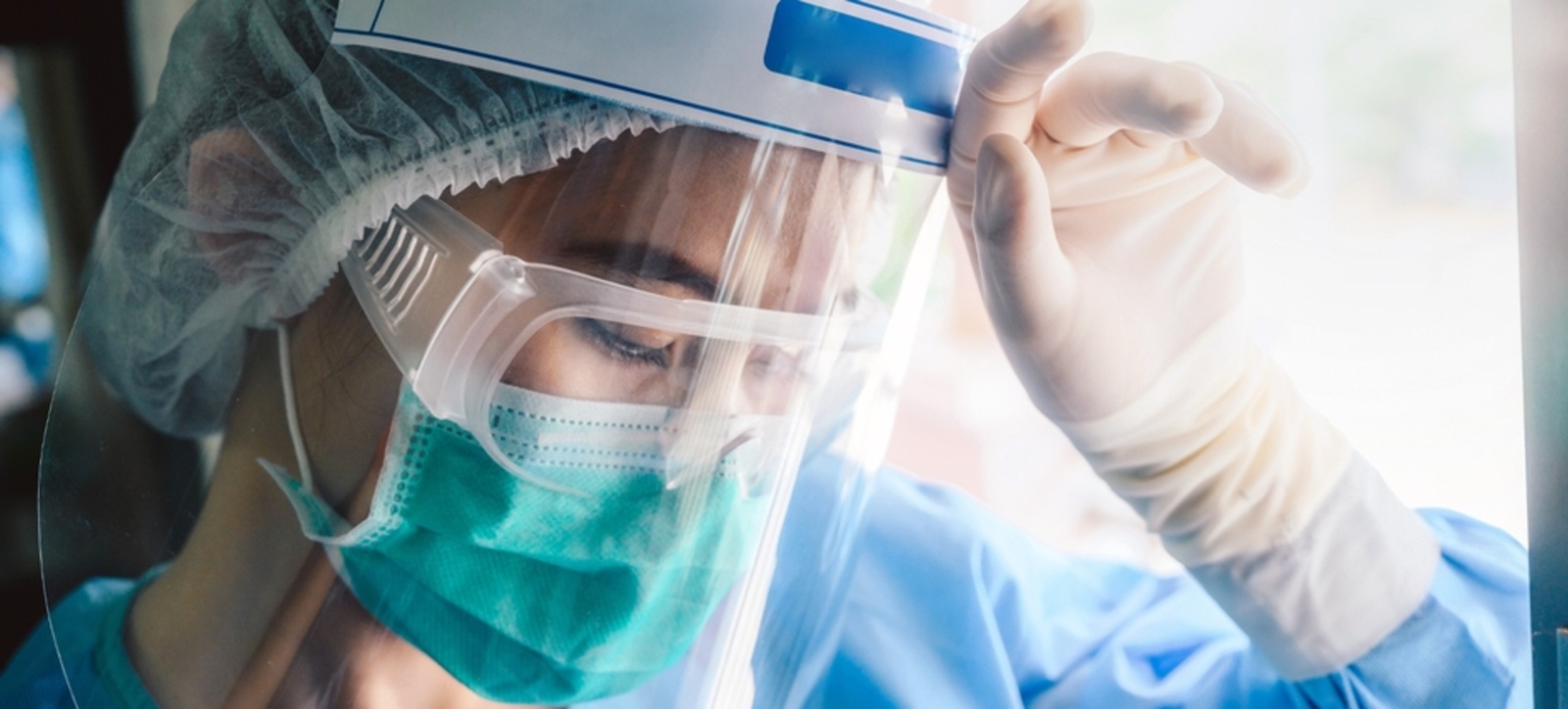 A female medical worker dressed in PPE holding her hand up to her forehead.