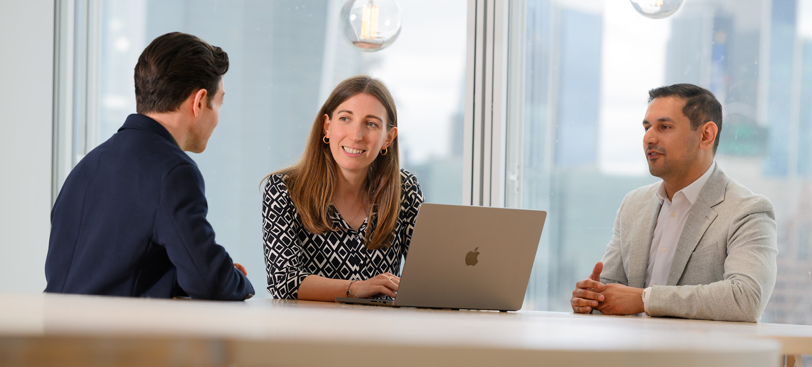 A woman and two men around a laptop studying for the Executive MBA