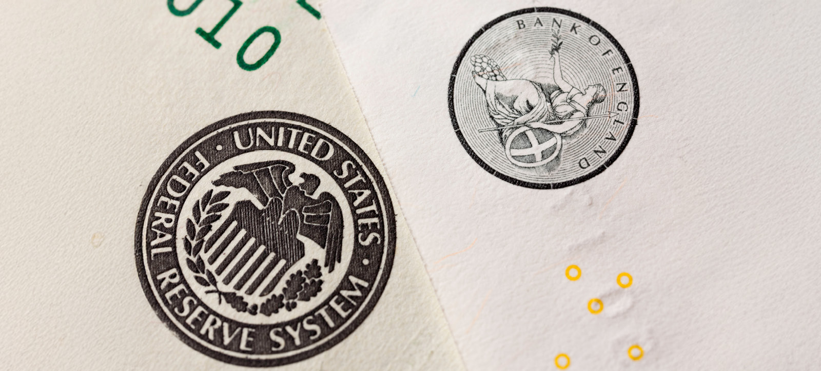 Two white envelopes laid overlapping each other. One is stamped with the Bank of England seal and the other is stamped with the US Federal Reserve symbol.