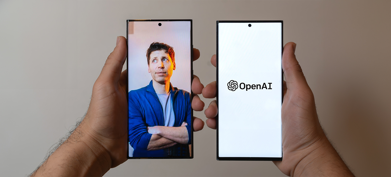 Two hands, each holding a mobile phone. One shows a photograph of ChatGPT creater Sam Altman stood with his sleeves rolled up and arms crossed, the other shows the OpenAI logo.