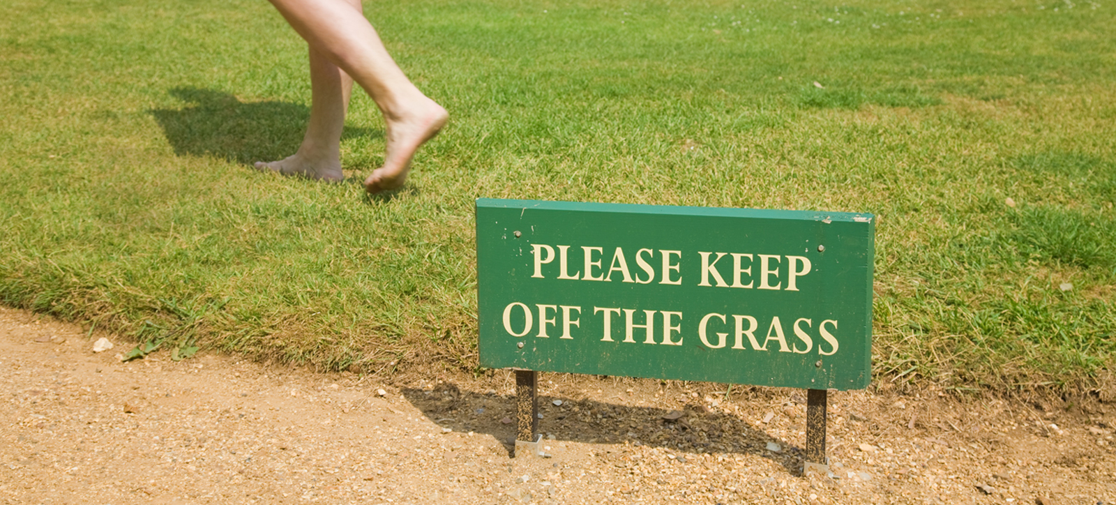 A person walking on some grass behind a sign which states A person walking on some grass behind a sign which states