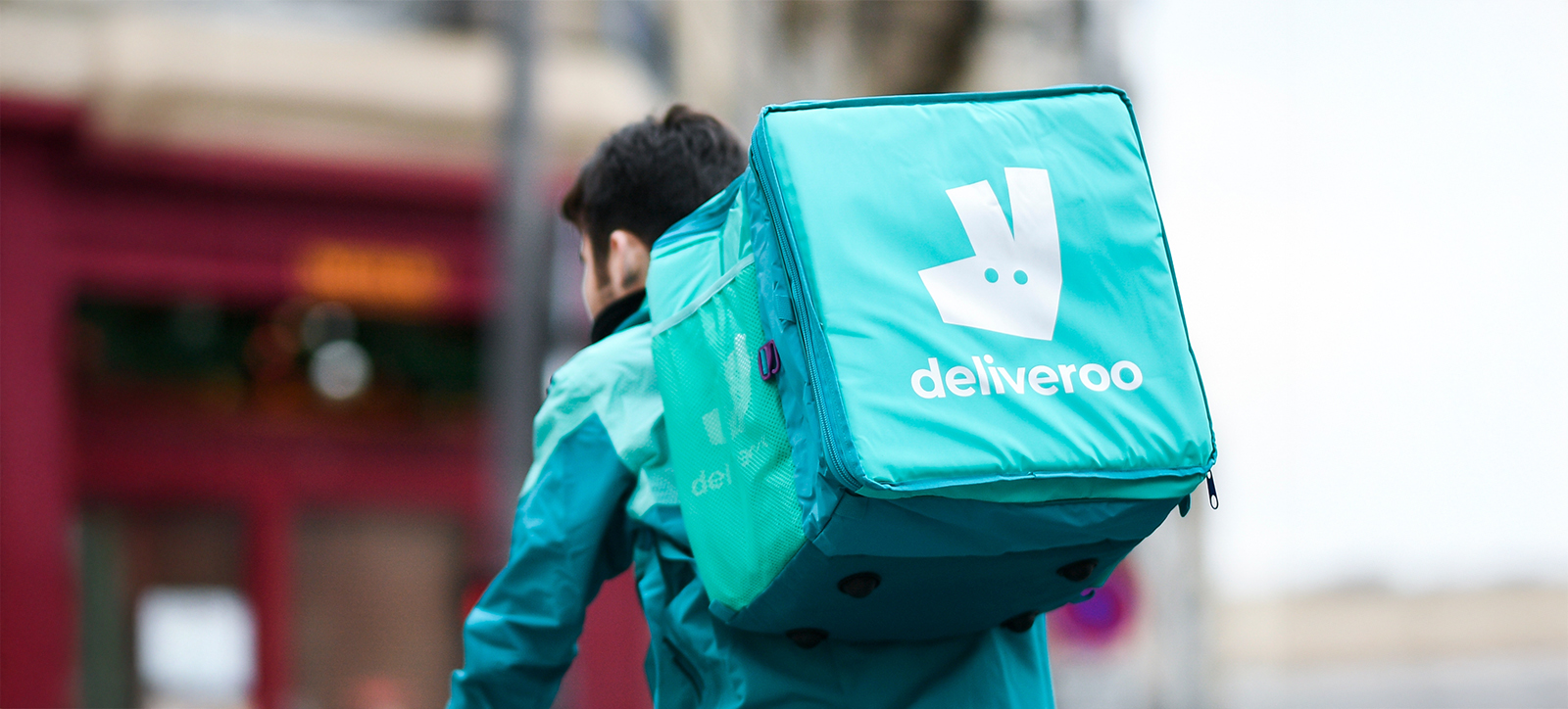 A photograph of Deliveroo delivery rider, taken from behind, showing the food delivery box on their back.