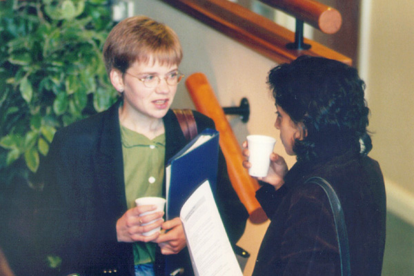 Two students holding cups and documents talking to each other.