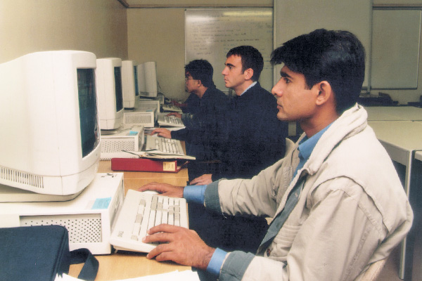 Three men sat at a desk working on desktop computers.